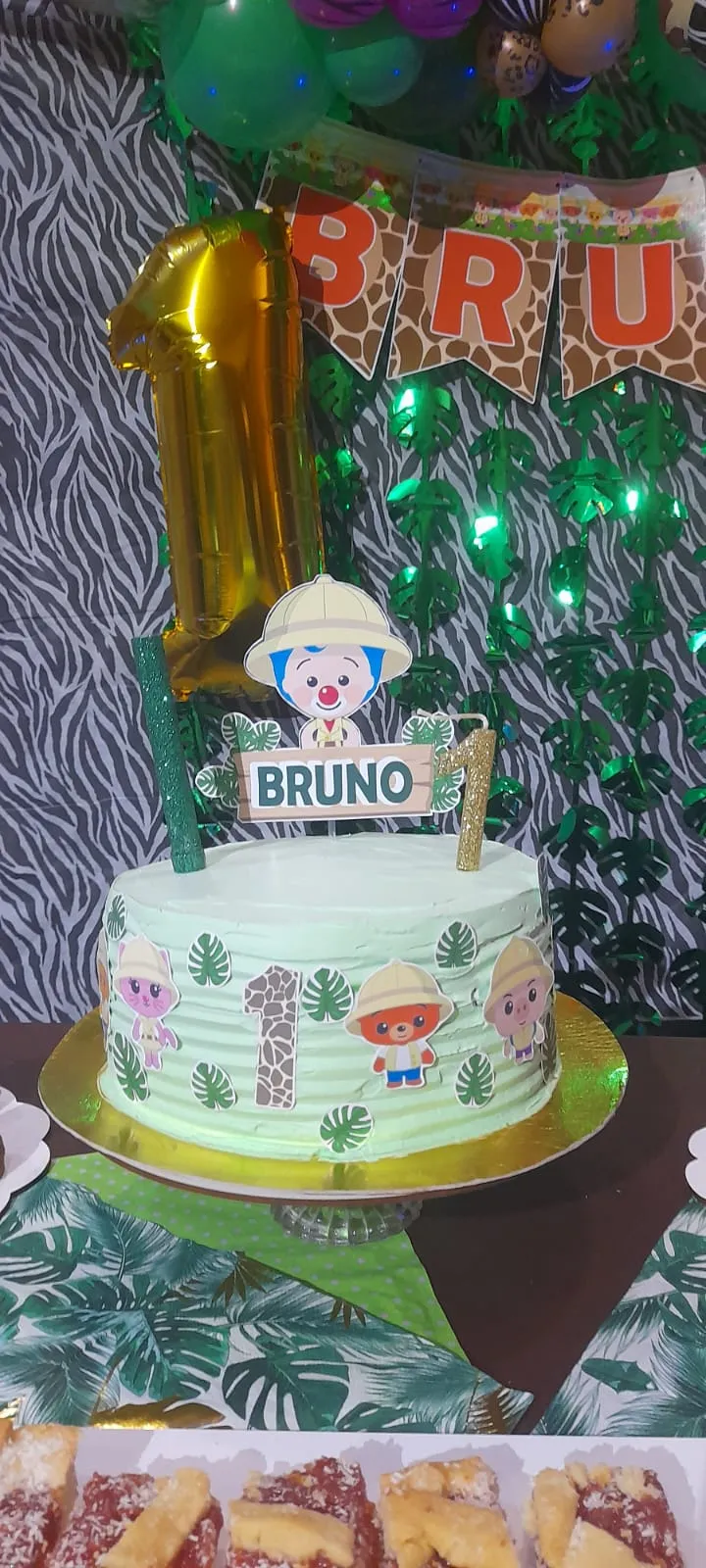 Torta de cumpleaños verde agua con motivos de selva, muñequitos y un cartel con el nombre Bruno, servida en la mesa dulce del cumpleaños.